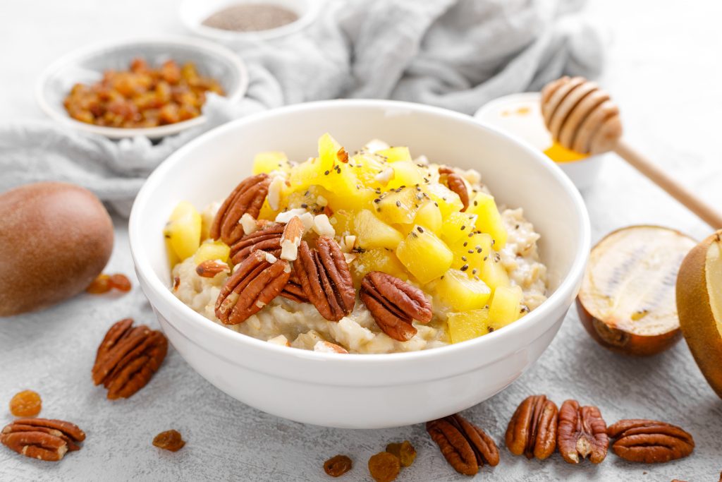 Oatmeal porridge with kiwi fruit, pecan nuts and honey in bowl for breakfast