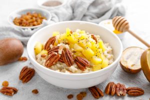 Oatmeal porridge with kiwi fruit, pecan nuts and honey in bowl for breakfast