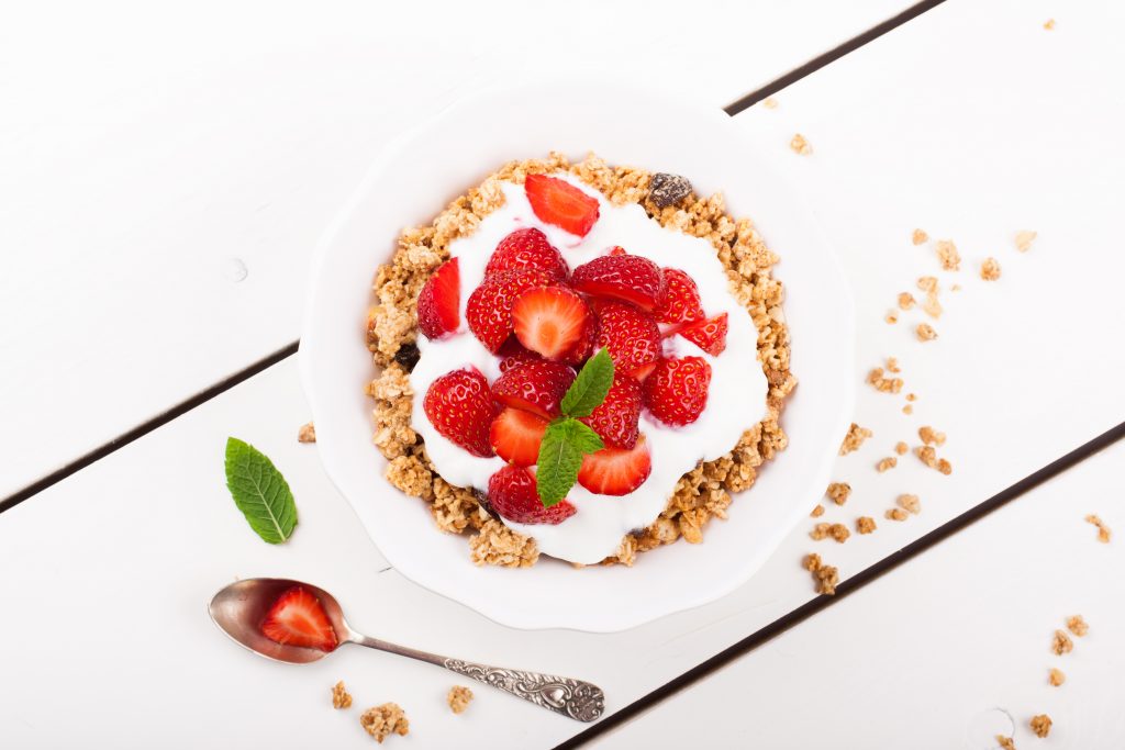 Yogurt with homemade granola or muesli and fresh strawberries for healthy morning breakfast, selective focus, over white. Healthy food background. Top view.